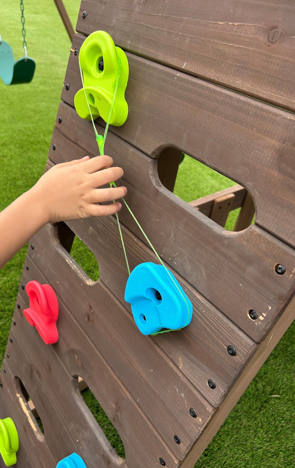 Child stretching a band between climbing holds on a backyard rock wall during play-based speech therapy in San Diego