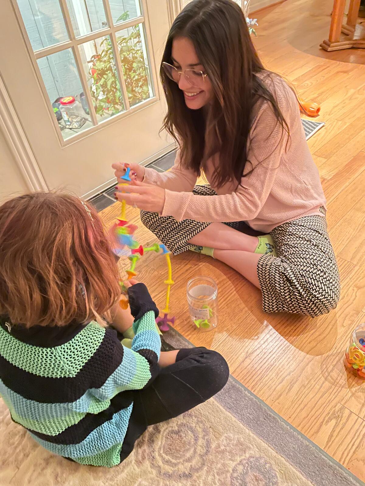 Alyssa Pitts and a child building with Squigz suction toys during play-based articulation therapy